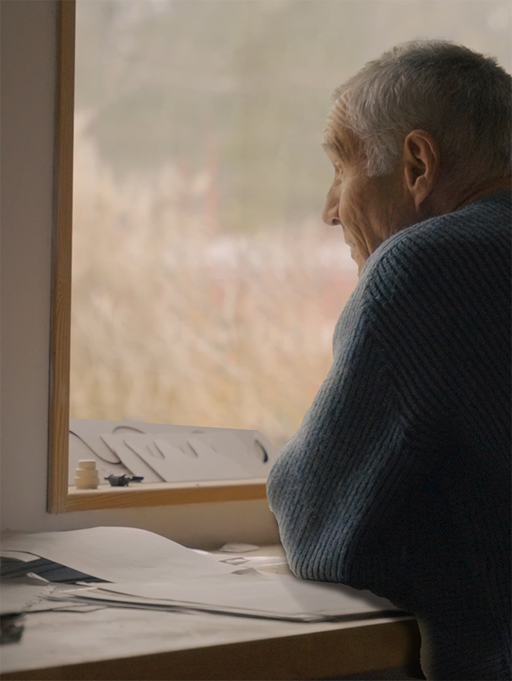 Elderly man gazes out window from studio desk during Deben Estuary community project