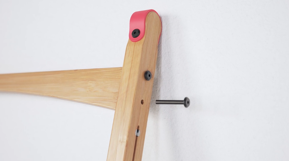 Close-up of a wooden desk frame being mounted to a white wall, showing black screws and a red plastic corner cap for secure wall attachment.