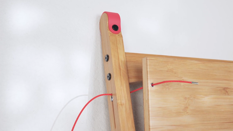 Close-up of a wooden wall-mounted desk showing red cord being threaded through holes to secure the fold-down surface in place.