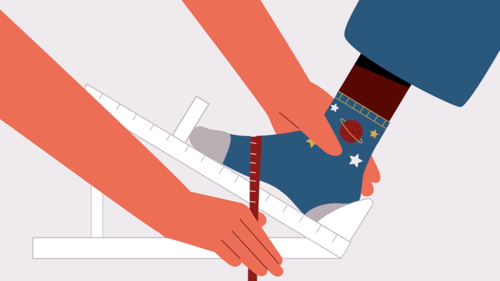 Child's foot in space-themed sock being measured using a foot gauge held by an adult.