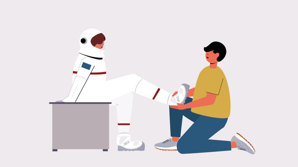 Person kneeling to help astronaut put on customized footwear as they sit on a bench.