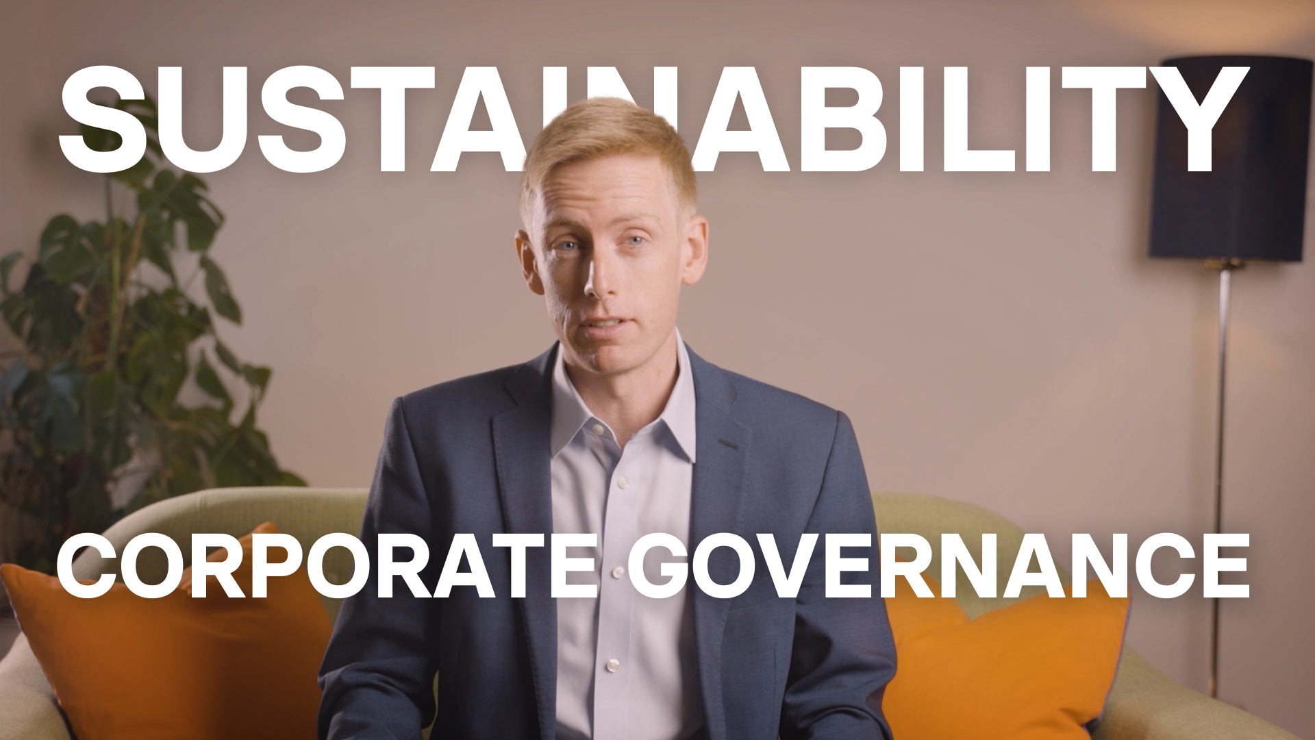 A man in a suit sits on a green sofa with orange cushions, speaking in an interview setting, with large overlay text reading “SUSTAINABILITY” and “CORPORATE GOVERNANCE” behind him.