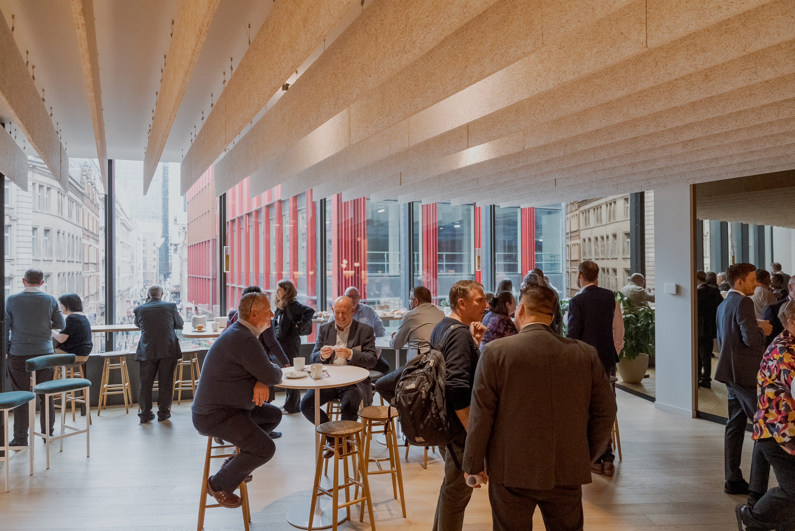 People networking and having conversations in a modern indoor event space with large windows overlooking a city street.