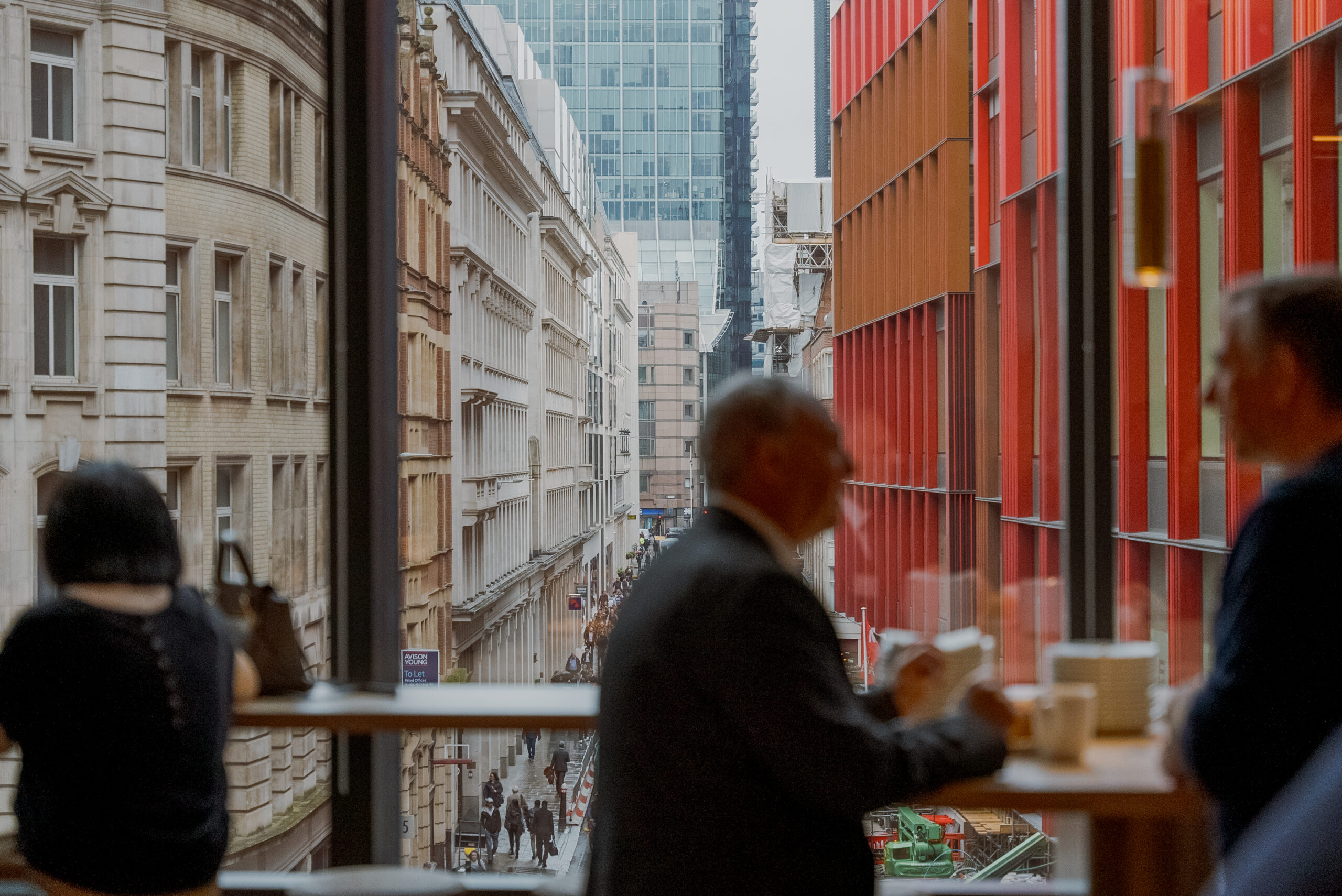 View of a busy London street framed by large windows, with silhouettes of people talking over coffee in the foreground at a conference venue.