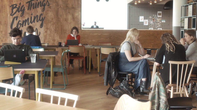 People working and collaborating in a bright, modern WeWork space with wooden floors, colorful furniture, and a motivational mural reading "Big Things Coming" on the wall.